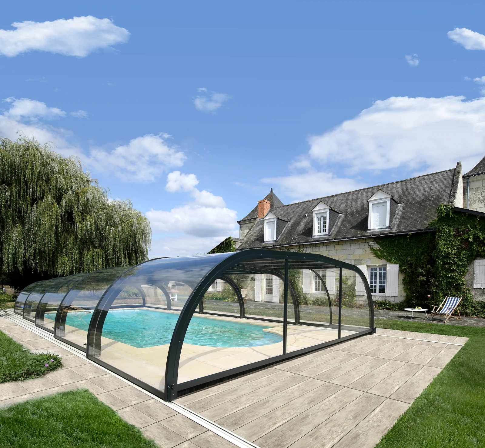 Abri de piscine bas et cintré installé autour d’un bassin dans un jardin