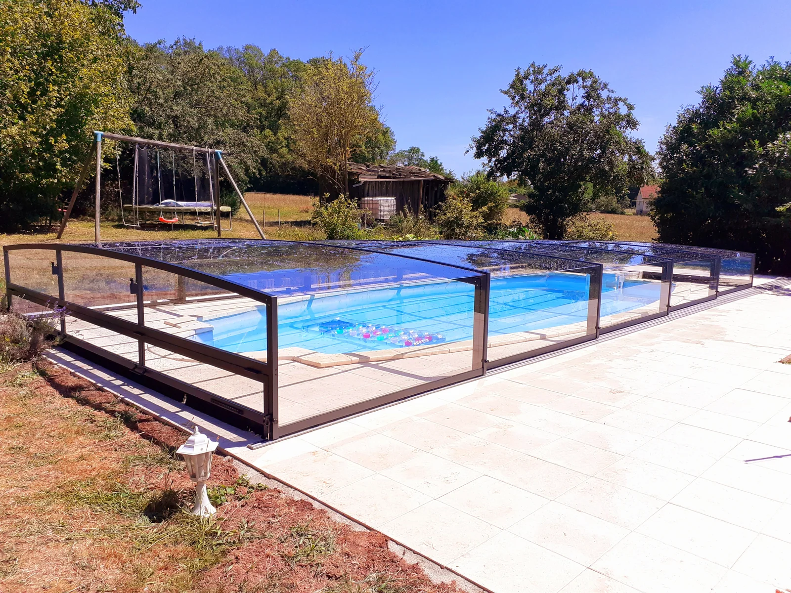 Abri de piscine bas à panneaux transparents sur une terrasse claire