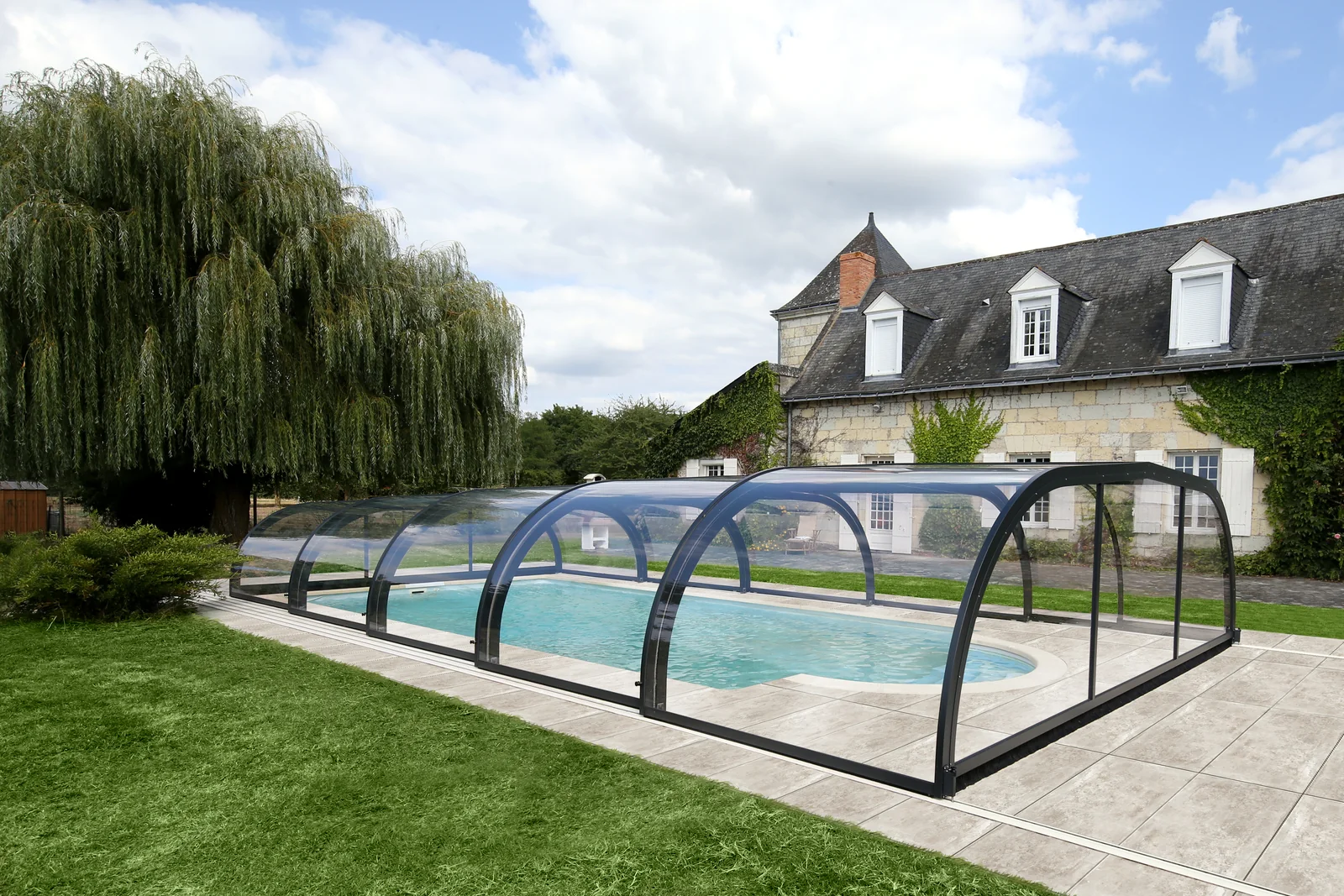 Abri de piscine bas à modules cintrés sur une terrasse en pierre