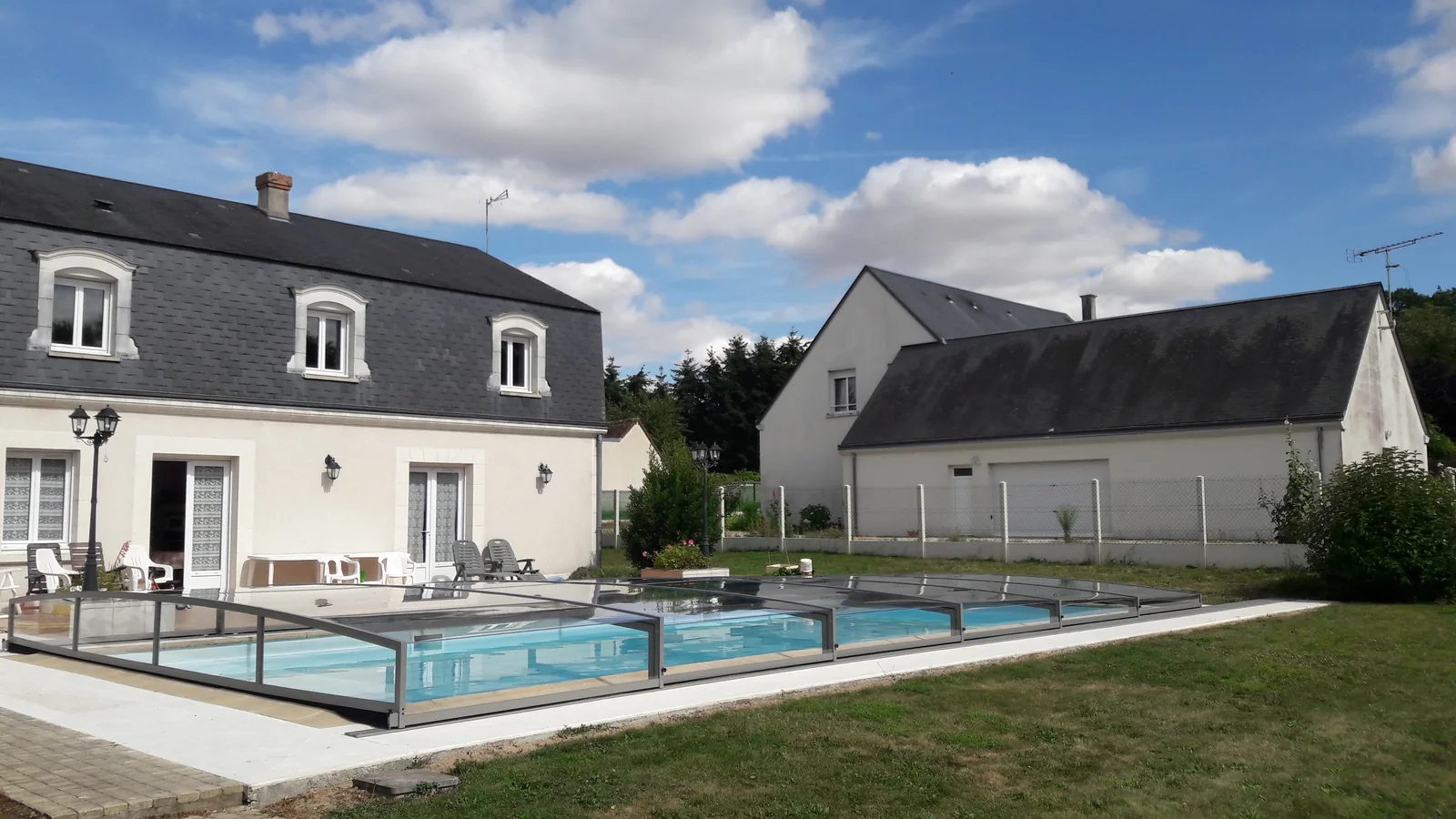 Abri de piscine bas installé devant une maison avec terrasse