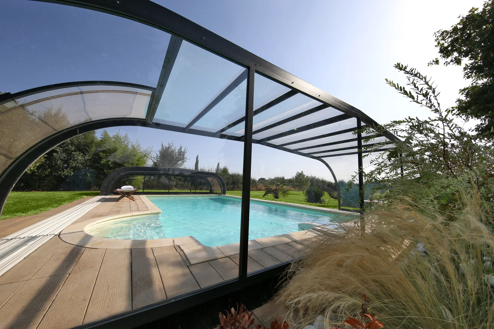 Abri de piscine haut à structure noire vu depuis la terrasse